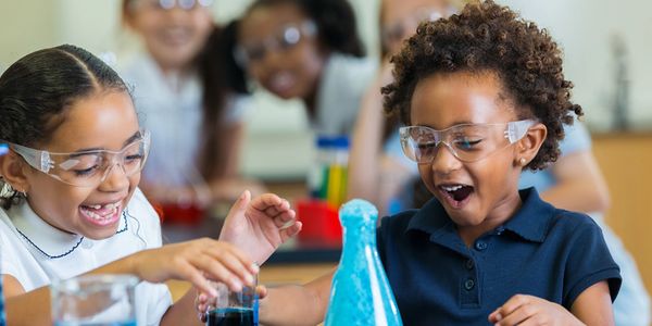 Two children laughing as a science experiment spills out of a beaker