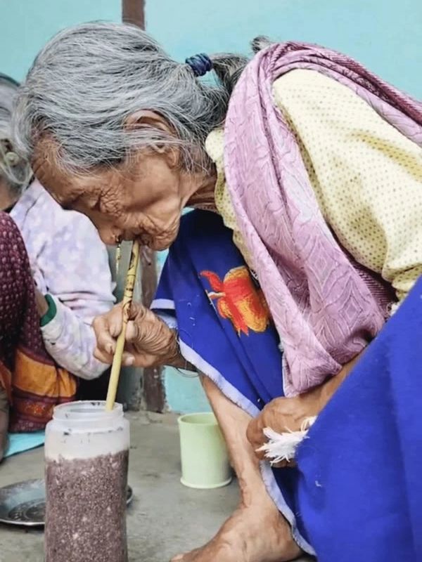 Elderly woman drinking traditional tongba from a vessel with a pipsing straw