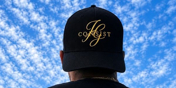 Person wearing a black cap with the word "CONSIST" against a blue sky.
