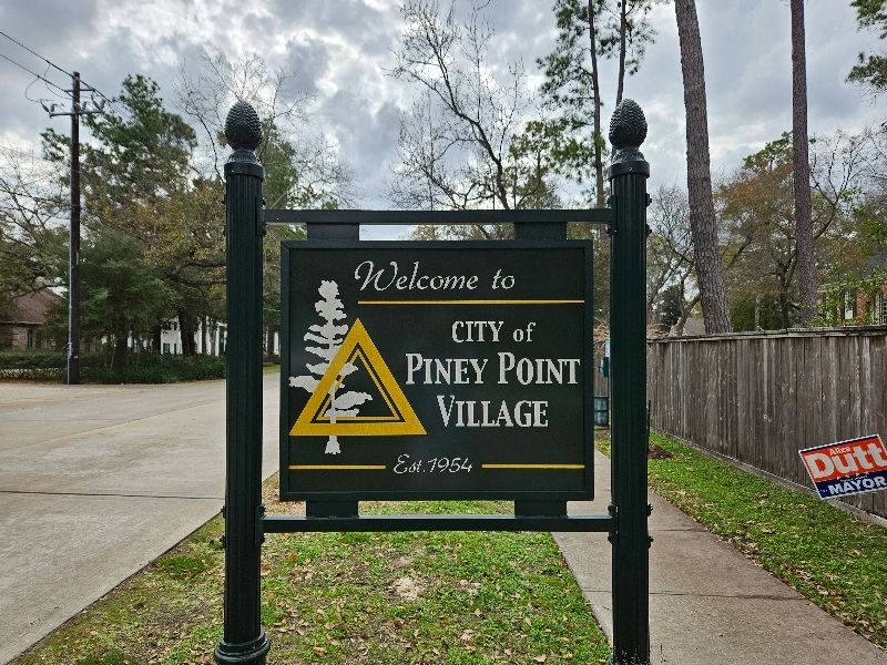 Welcome to City of Piney Point Village sign. A green sign with a tree and yellow triangle.