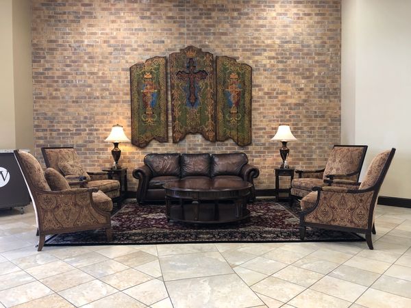 Brown leather couch and four tan armchairs in front of a hanging cross in a church.