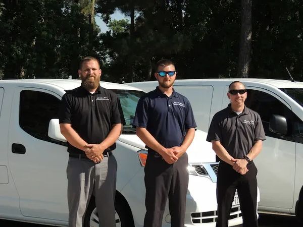 Three expert fabric cleaning technicians standing in front of two service vans.