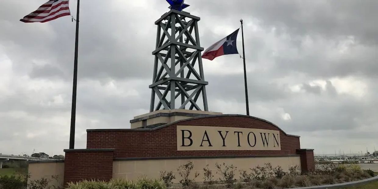 The Baytown city sign with an oil rig and an American flag and Texas flag on either side in Baytown,