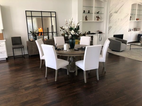 Six white dining chairs around a round table in the middle of a large room.