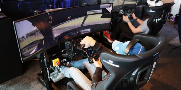 Two people using racing simulators with curved screens.