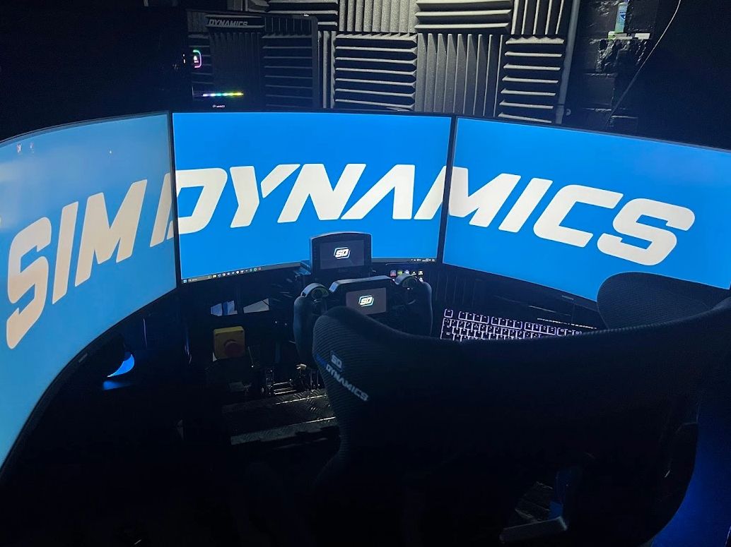 Curved triple-monitor racing simulator setup with SIM DYNAMICS branding.
