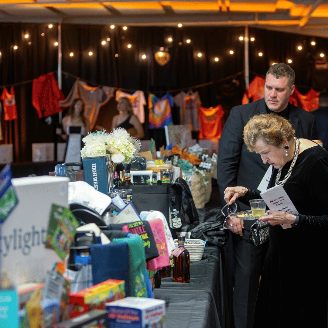Woman holding glasses looking at silent auction items while man stands next to her