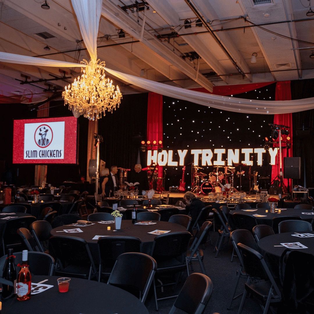 Banquet room with black tables and chairs, chandelier and lighted sign with words Holy Trinity
