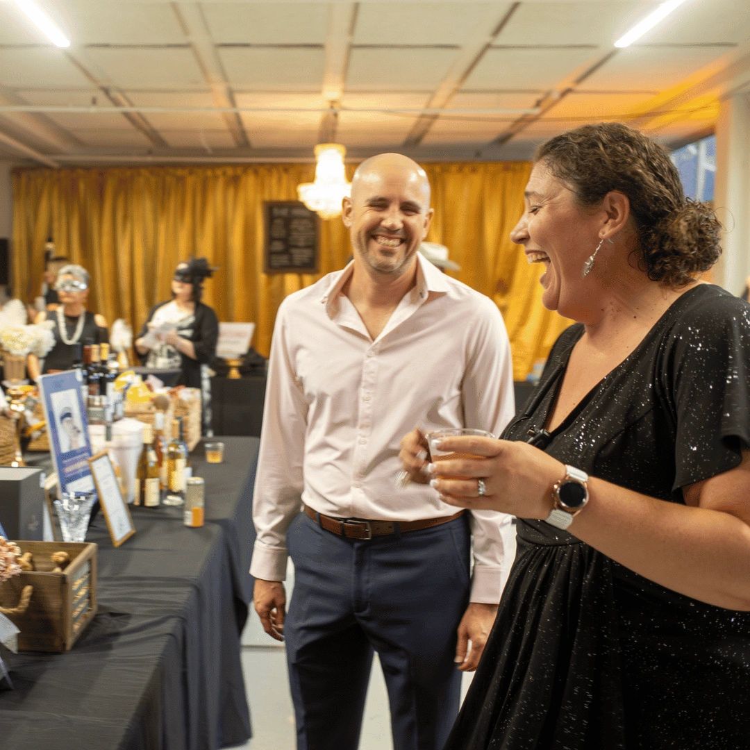 Man and woman laughing next to silent auction table