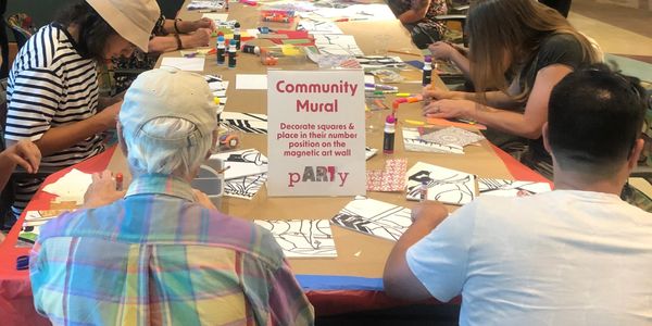 People creating art for a community mural event at a long table.