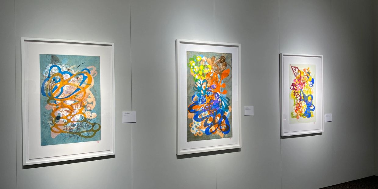 Three colorful abstract paintings displayed in a gallery with white walls and frames.