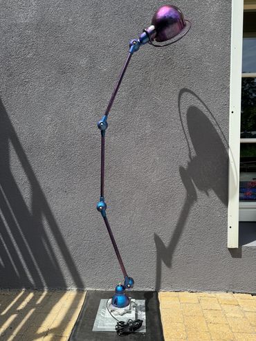 Lampe articulée violette avec ombre projetée sur un mur gris.