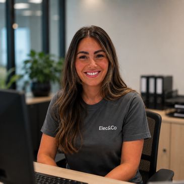 Smiling woman in Elec&amp;Co t-shirt sitting at office desk.