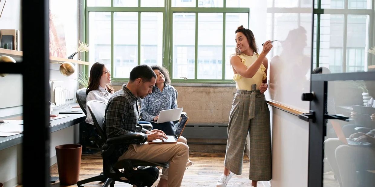 A woman presents ideas on a whiteboard to colleagues in a modern office.