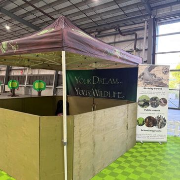 Indoor wildlife-themed booth setup with a tent and promotional banner.