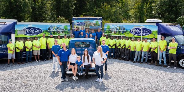 Large plumbing company team posing with branded trucks and a vintage blue car outdoors.
