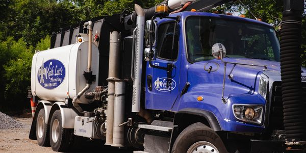 Blue and white Keith Lott's Plumbing truck parked on gravel.