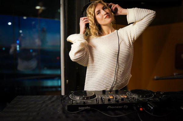 Woman DJ enjoying music while mixing tracks in a dimly lit room.