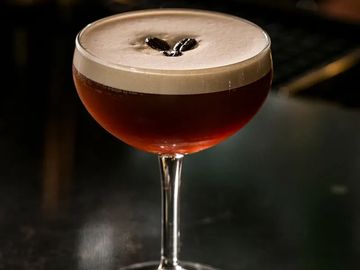 A cocktail with creamy foam and coffee beans garnish in a coupe glass.