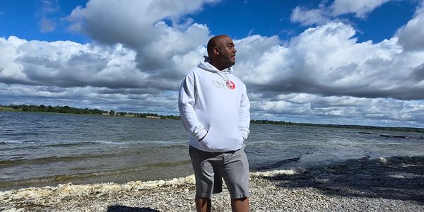 Randy Bowen smiling wearing a white United We Stand Canada hoodie at Sandbanks Provincial Park.