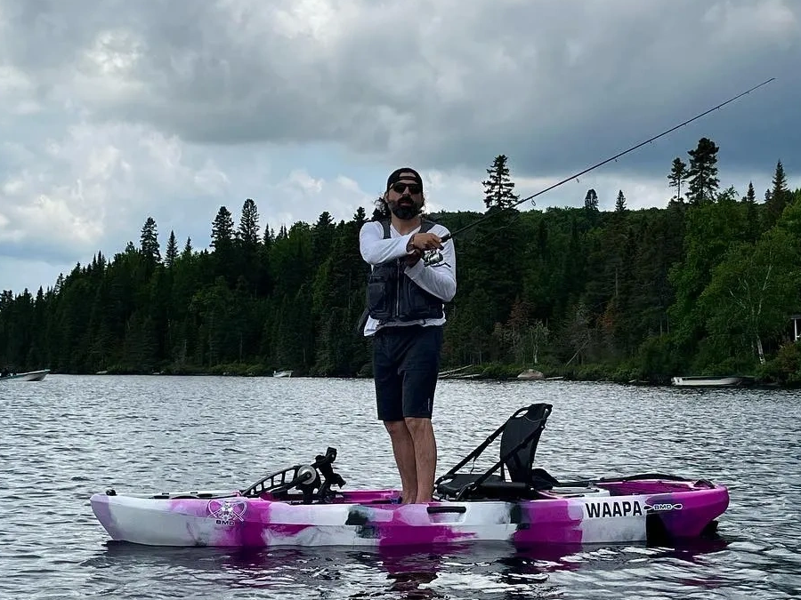 Homme en kayak rose pêche sur un lac calme.