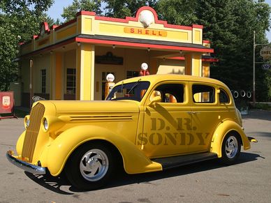 Yellow vintage car parked near an old Shell gas station.