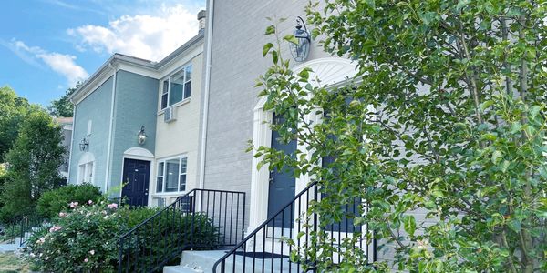 A row of townhouses with stairs leading to front doors surrounded by lush landscaping.