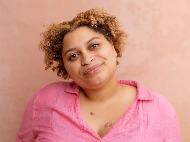 A headshot of Akili, a light-skinned Black woman with blonde curly hair wearing a pink shirt.