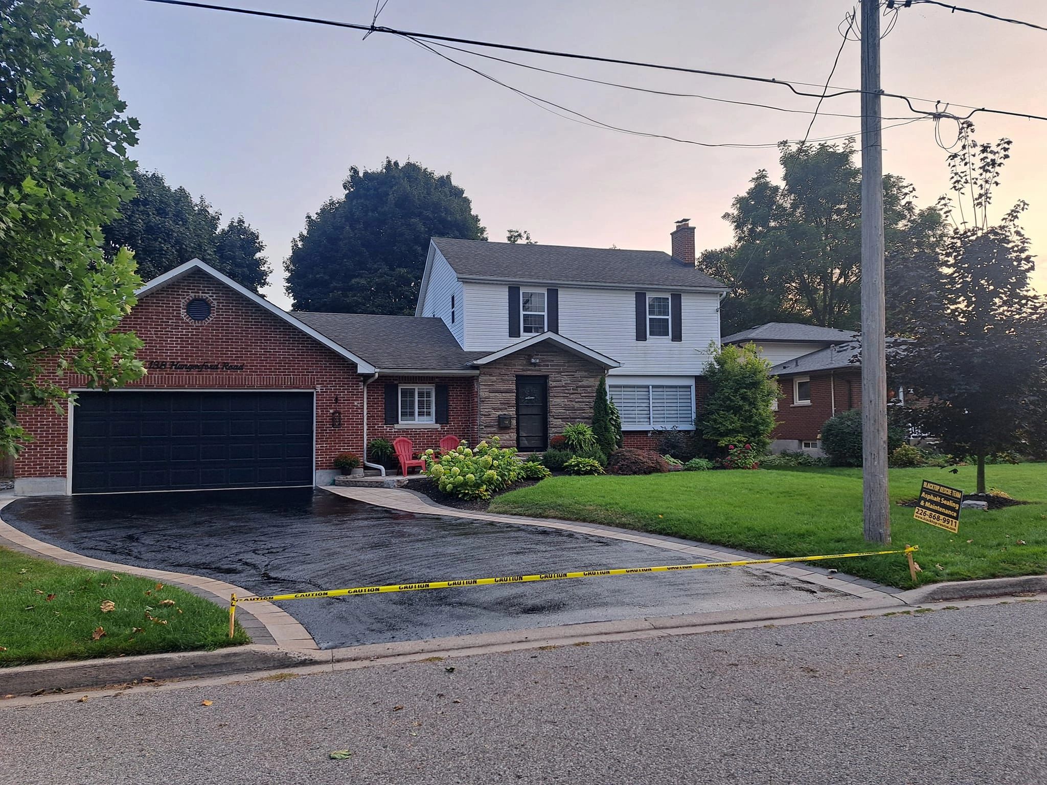 A freshly sealed driveway in front of a house with caution tape around it.