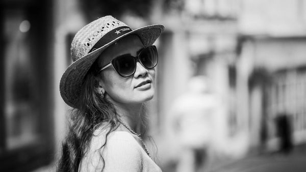 Woman wearing sunglasses and a straw hat smiling outdoors in black and white.