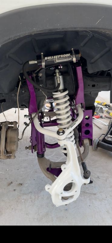 Close-up of custom vehicle suspension with white coilover and purple components.