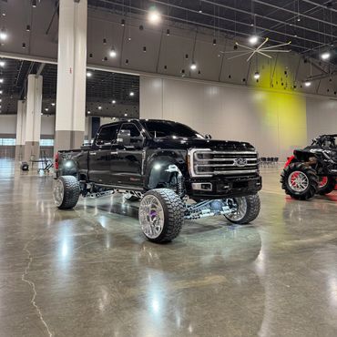 Black lifted Ford truck with illuminated underglow lights in an indoor showroom.