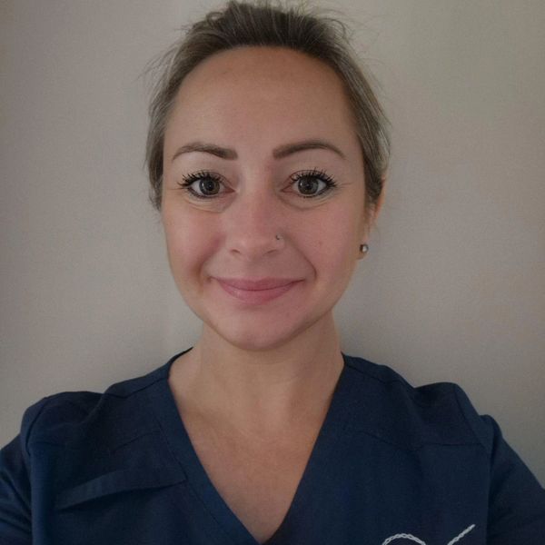 Smiling woman in navy blue scrubs with nose piercing.