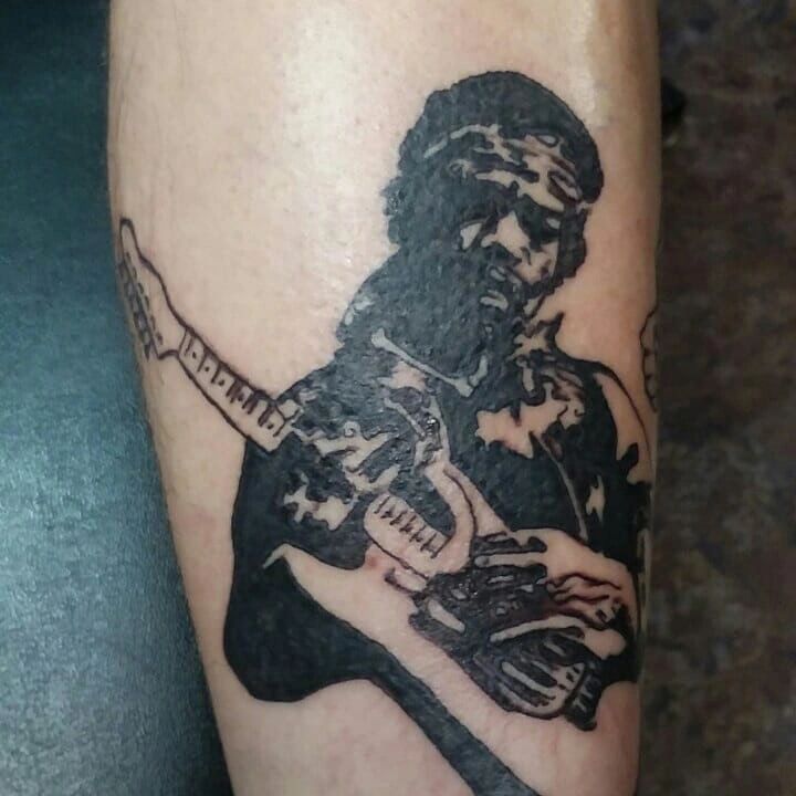Black ink tattoo of a person playing electric guitar