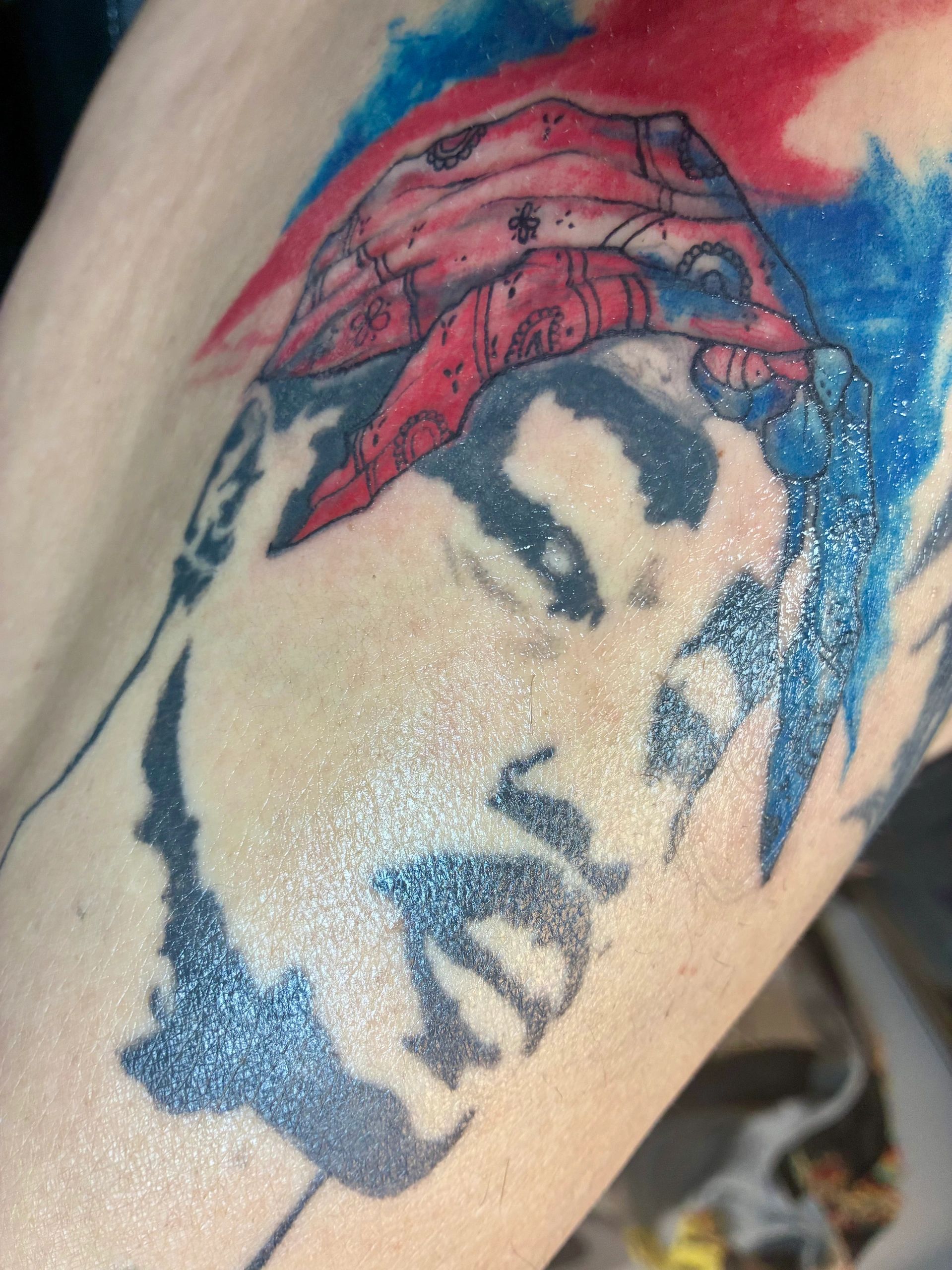 Tattoo of a face with a red bandana and blue accents