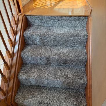 Carpeted stairs with wooden railings and sunlight on the floor.