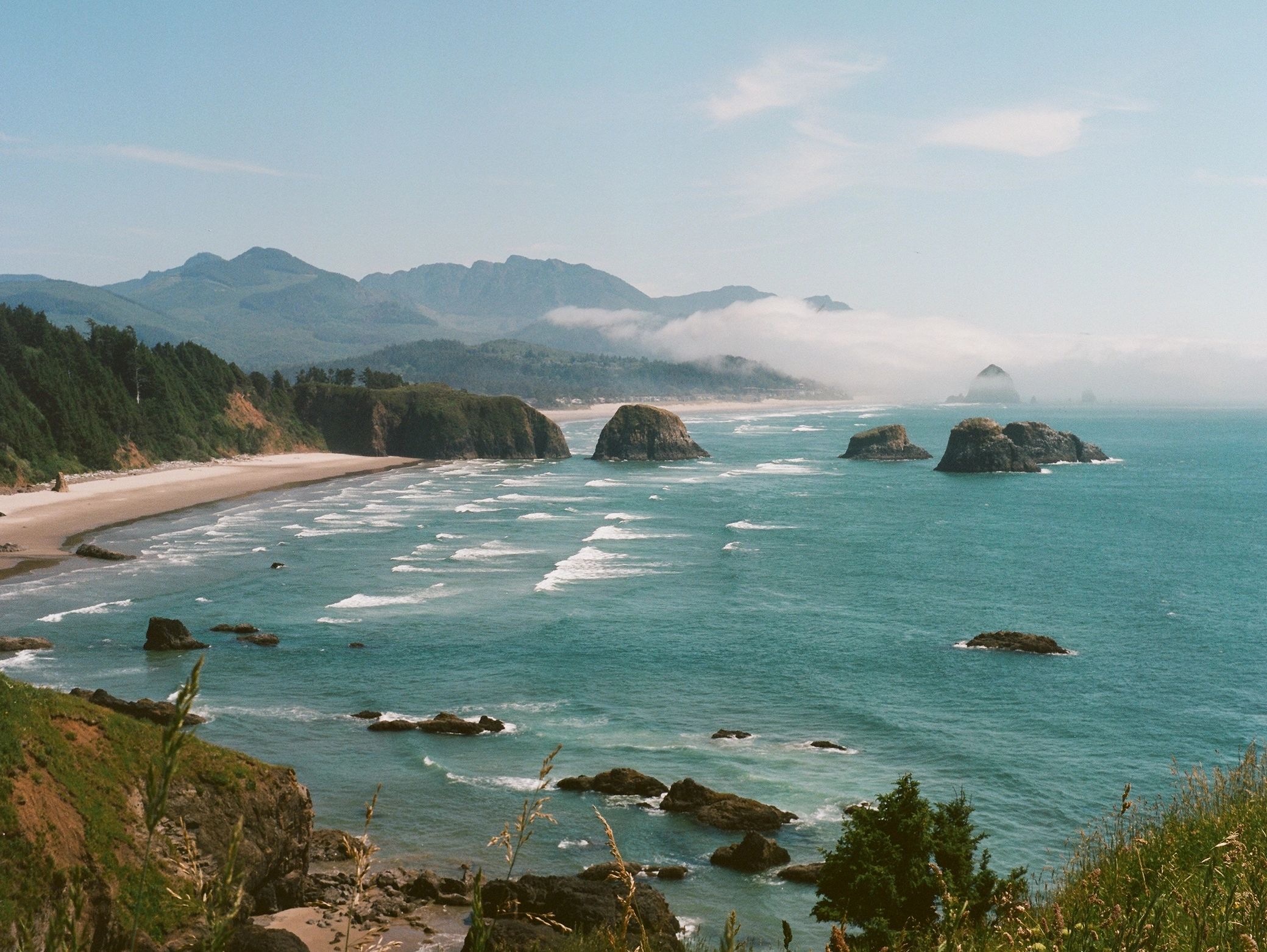 Rocky coastline with waves and distant mountains.
