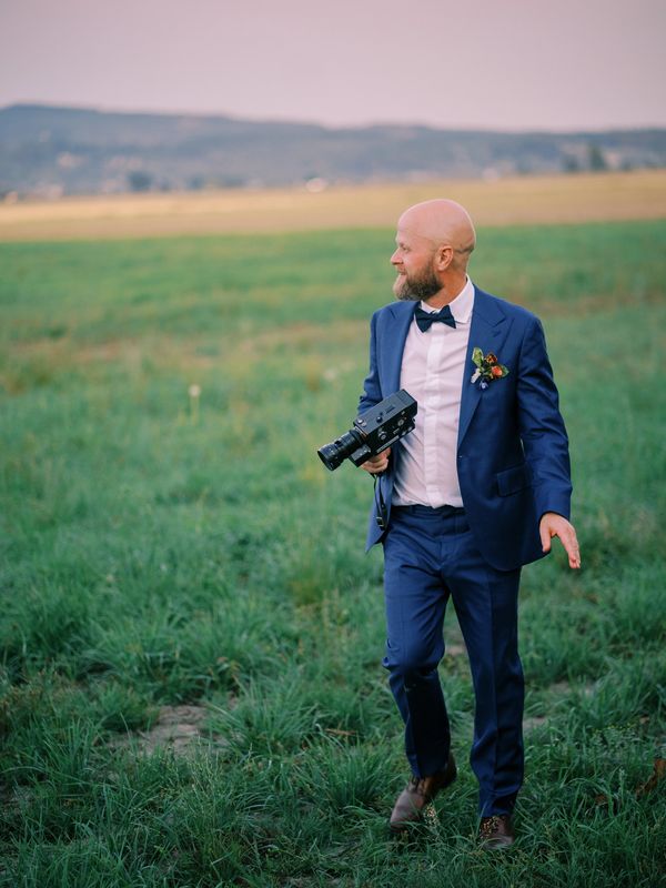 Man in a blue suit holding a vintage camera outdoors.