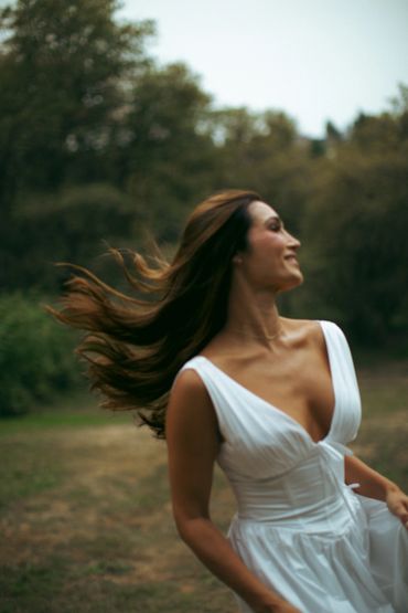 Woman in white dress spins outdoors with hair flowing.