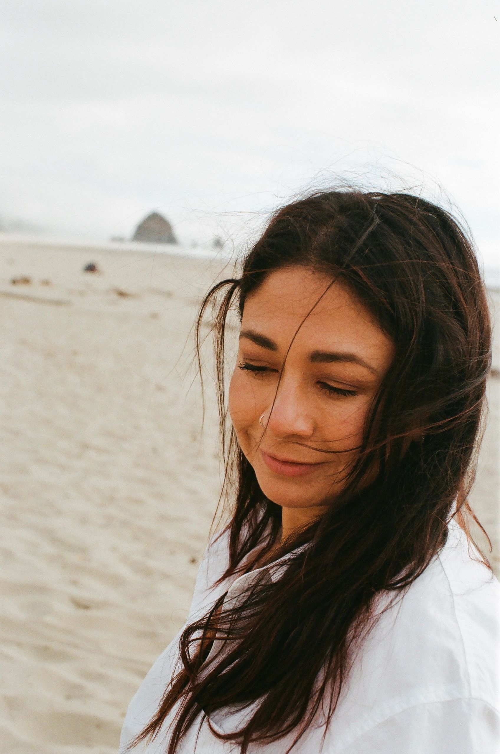 Woman smiling softly on a beach with wind-blown hair.