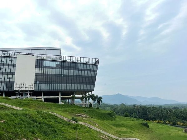 Modern glass building on a green hillside with mountains in the background.