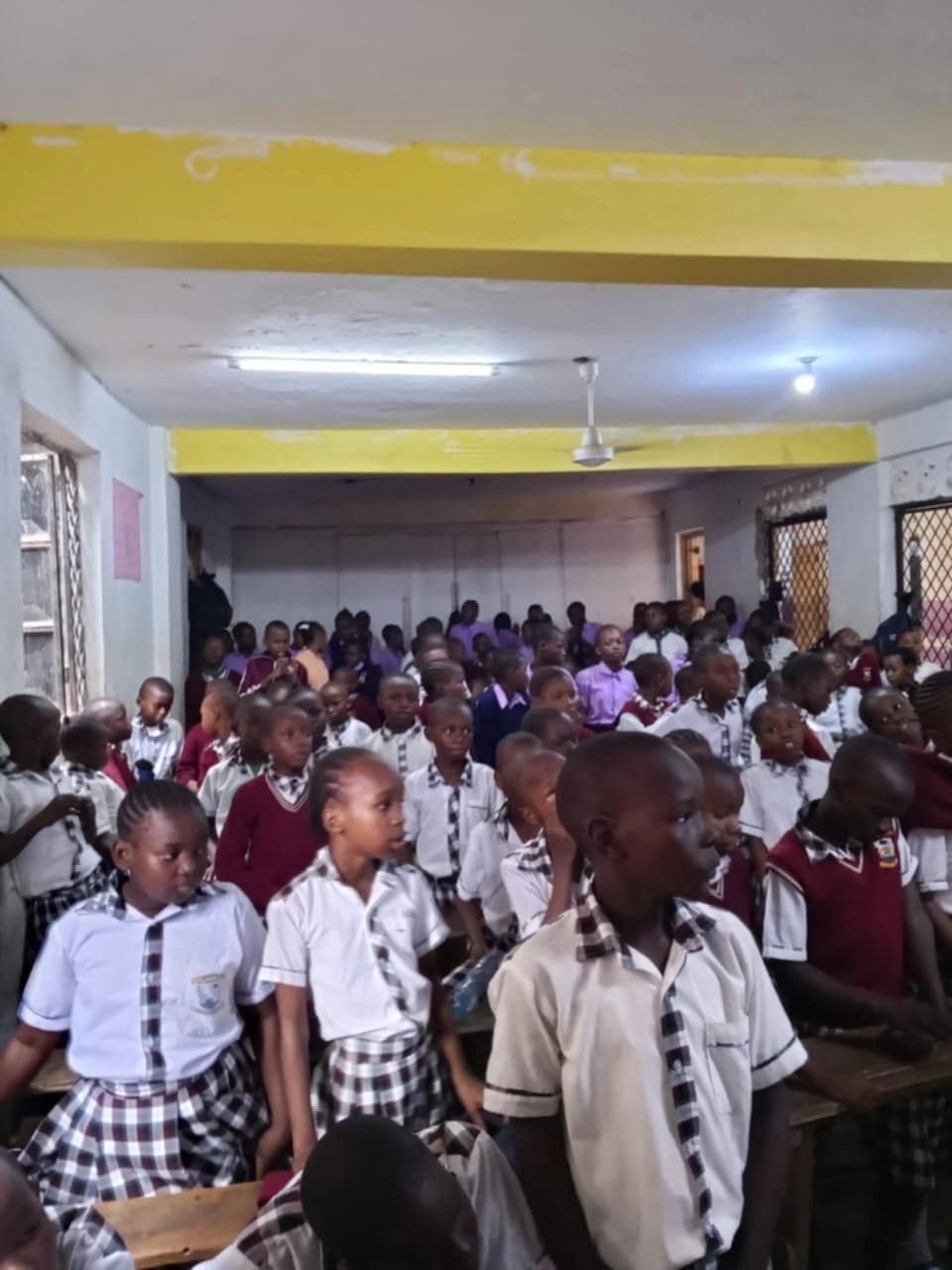A crowded classroom with students in school uniforms seated and standing.