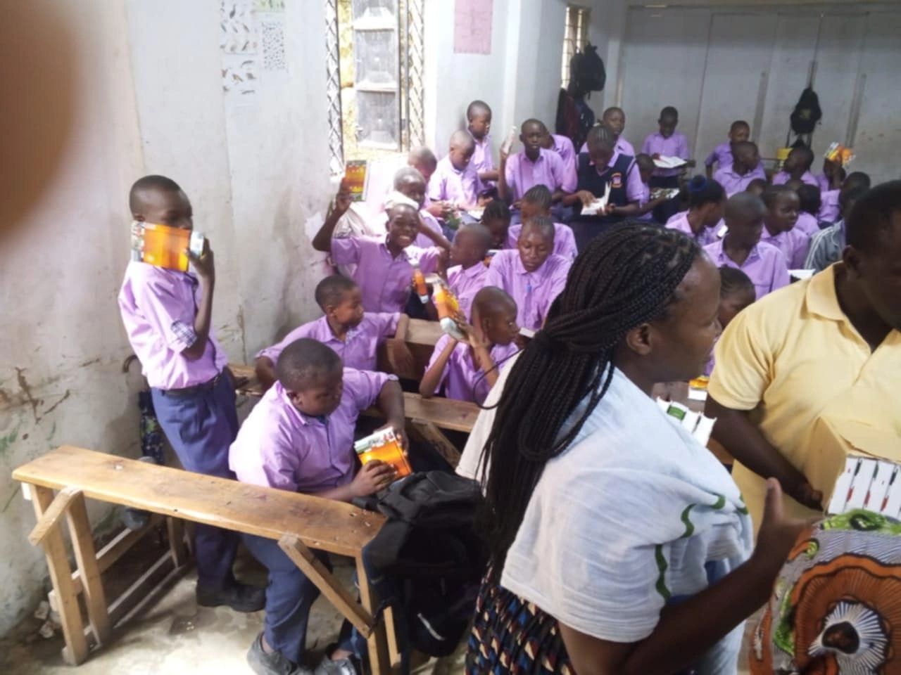 Schoolchildren in purple uniforms holding juice boxes in a crowded classroom.