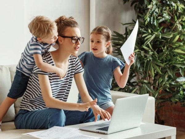 A mother working on a laptop with her two children beside her.