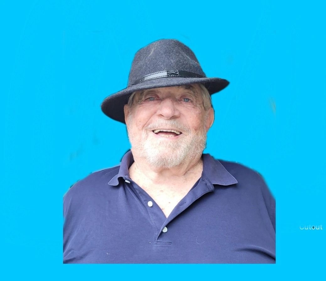 Smiling elderly man wearing a black hat and navy polo shirt against a bright blue background.