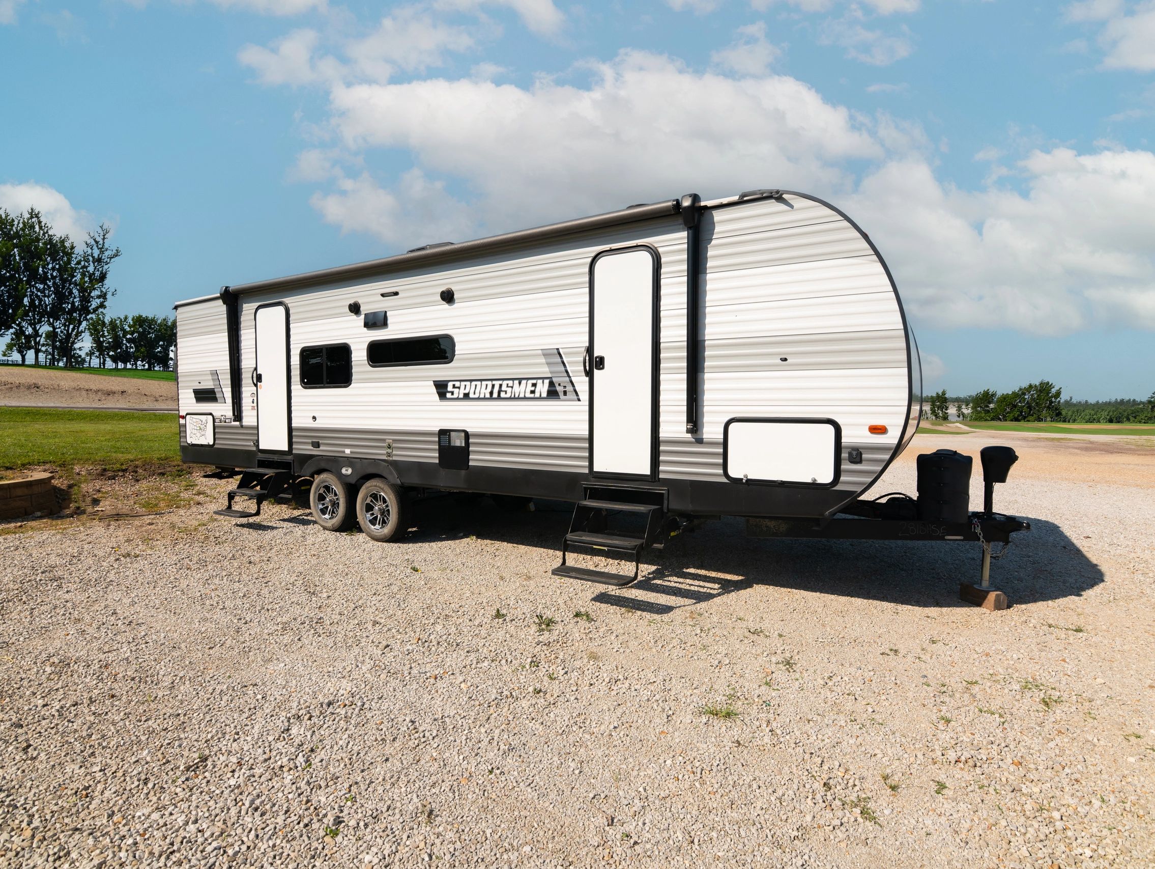 A white Sportsmen travel trailer parked on gravel under a blue sky.