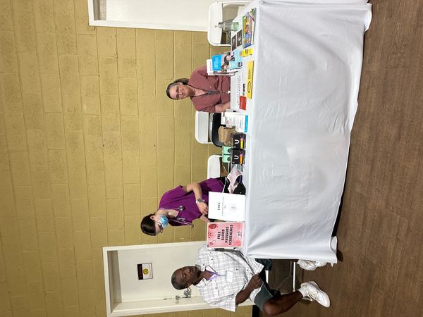 Three people at a health screening table indoors.