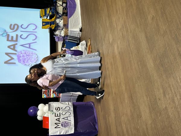 Two women posing on stage at a Mae's Oasis event.