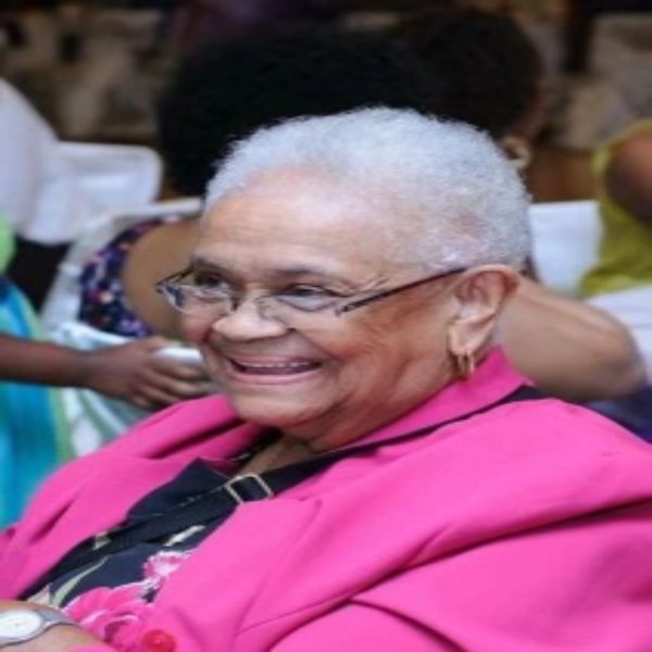 A beautiful elderly black woman with a pink jacket on smiling. 