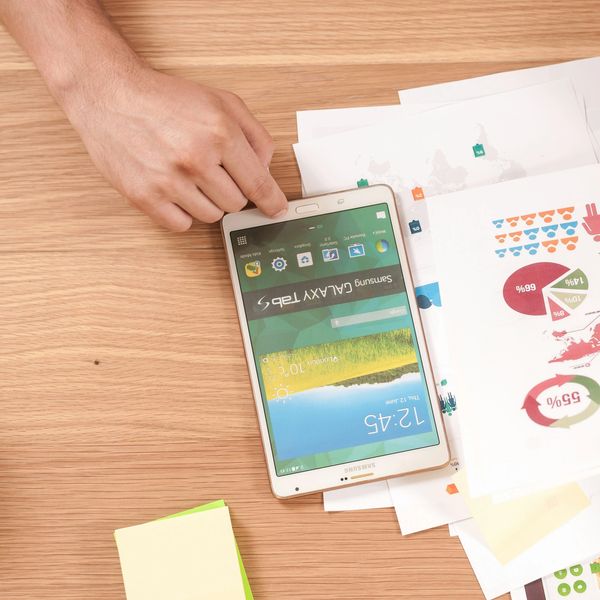 Hand holding a Samsung Galaxy Tab S on a desk with papers and sticky notes.